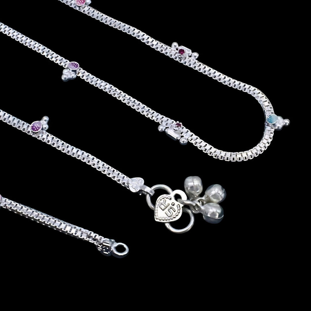 A top-down view of silver box-chain anklets placed on a solid black background.