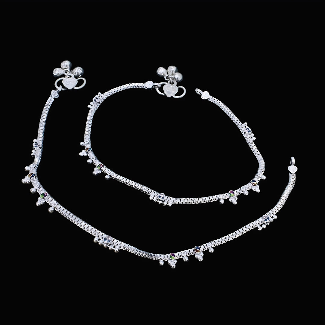 An overhead shot of a pair of ornate silver anklets, known as anklet, laid out against a solid black background.