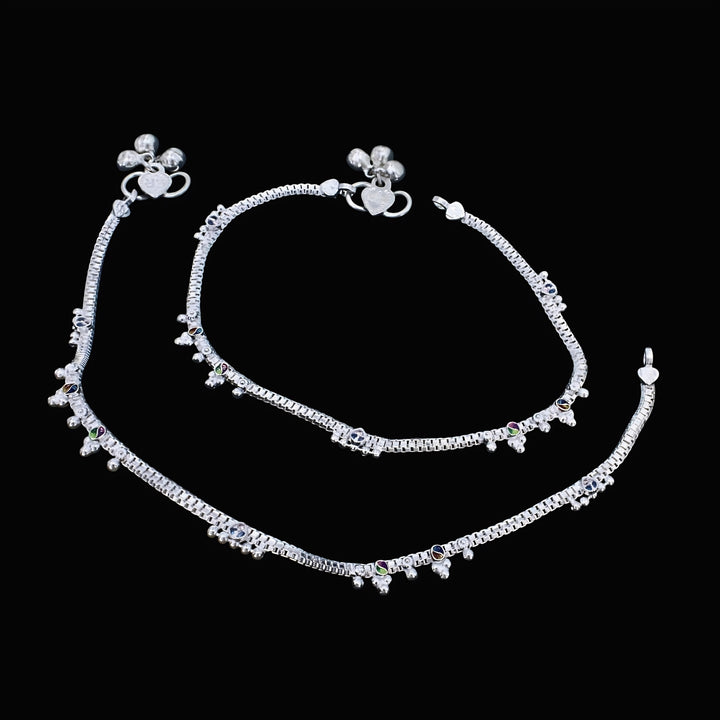 An overhead shot of a pair of ornate silver anklets, known as anklet, laid out against a solid black background.
