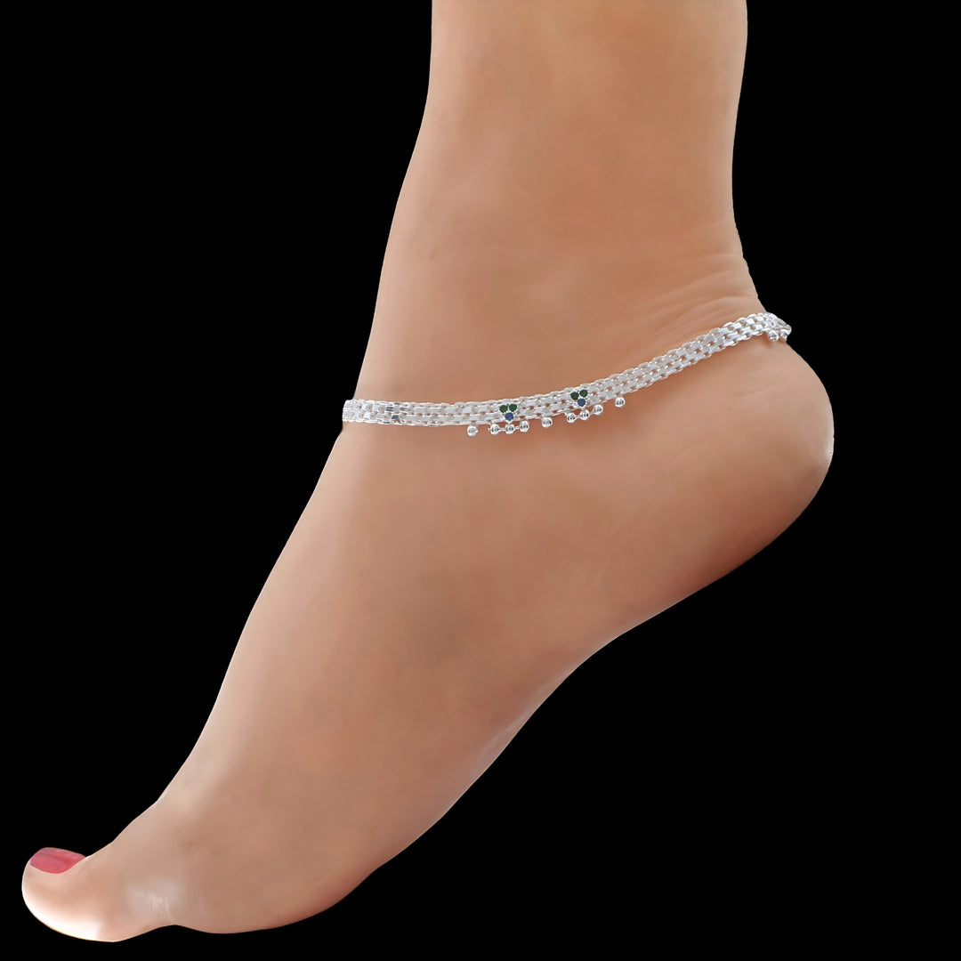 Elegant silver anklet with green and blue charms adorning a bare ankle against a black background.