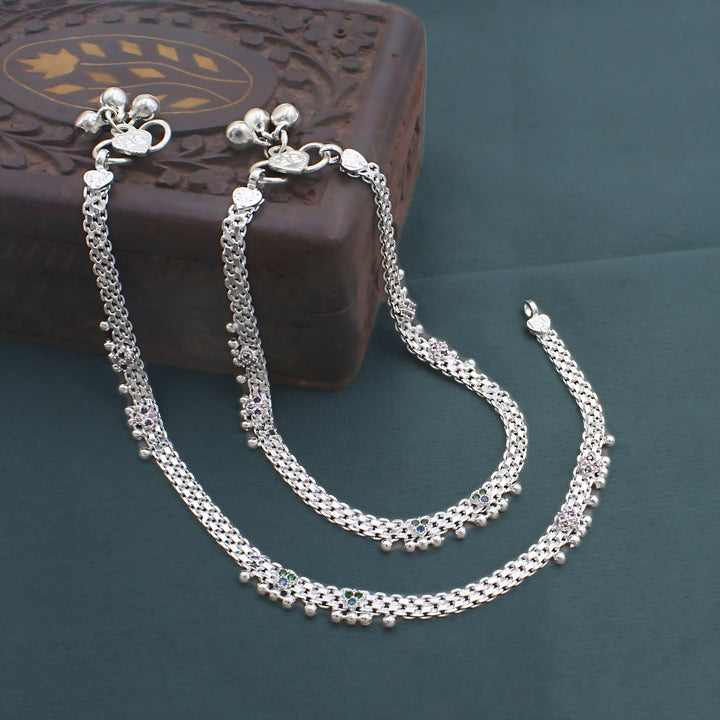 Traditional silver payal anklets with colorful stone accents and ghungroo bells elegantly displayed on a carved wooden box.