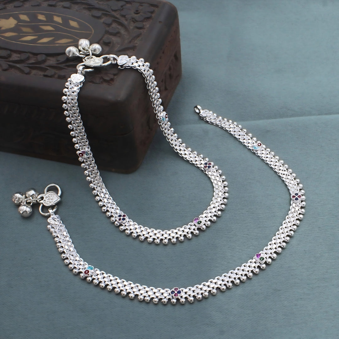 A pair of silver anklets with colorful flower patterns sits on a dark grey background.