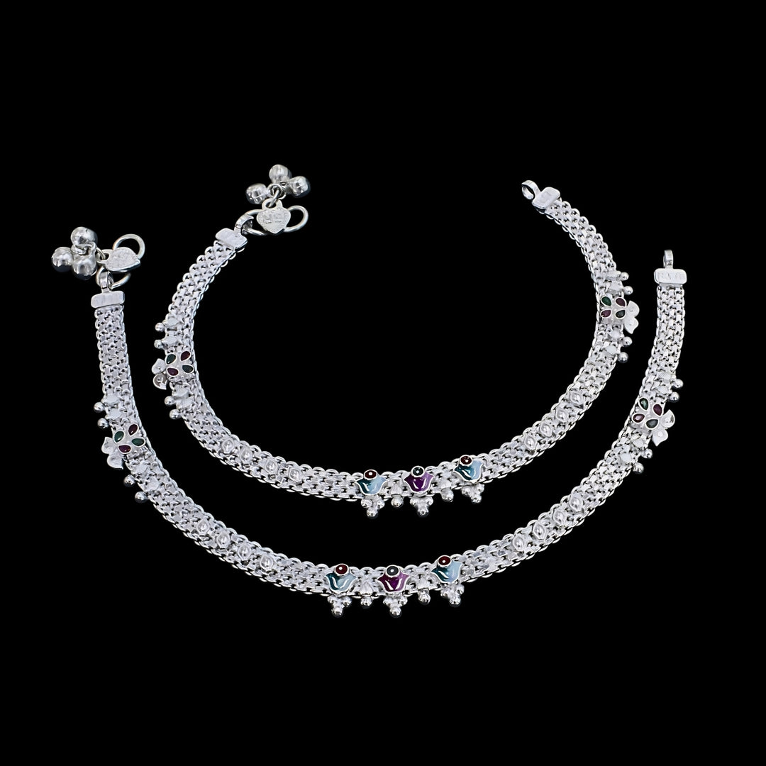 A pair of traditional silver anklets placed against a plain black background.