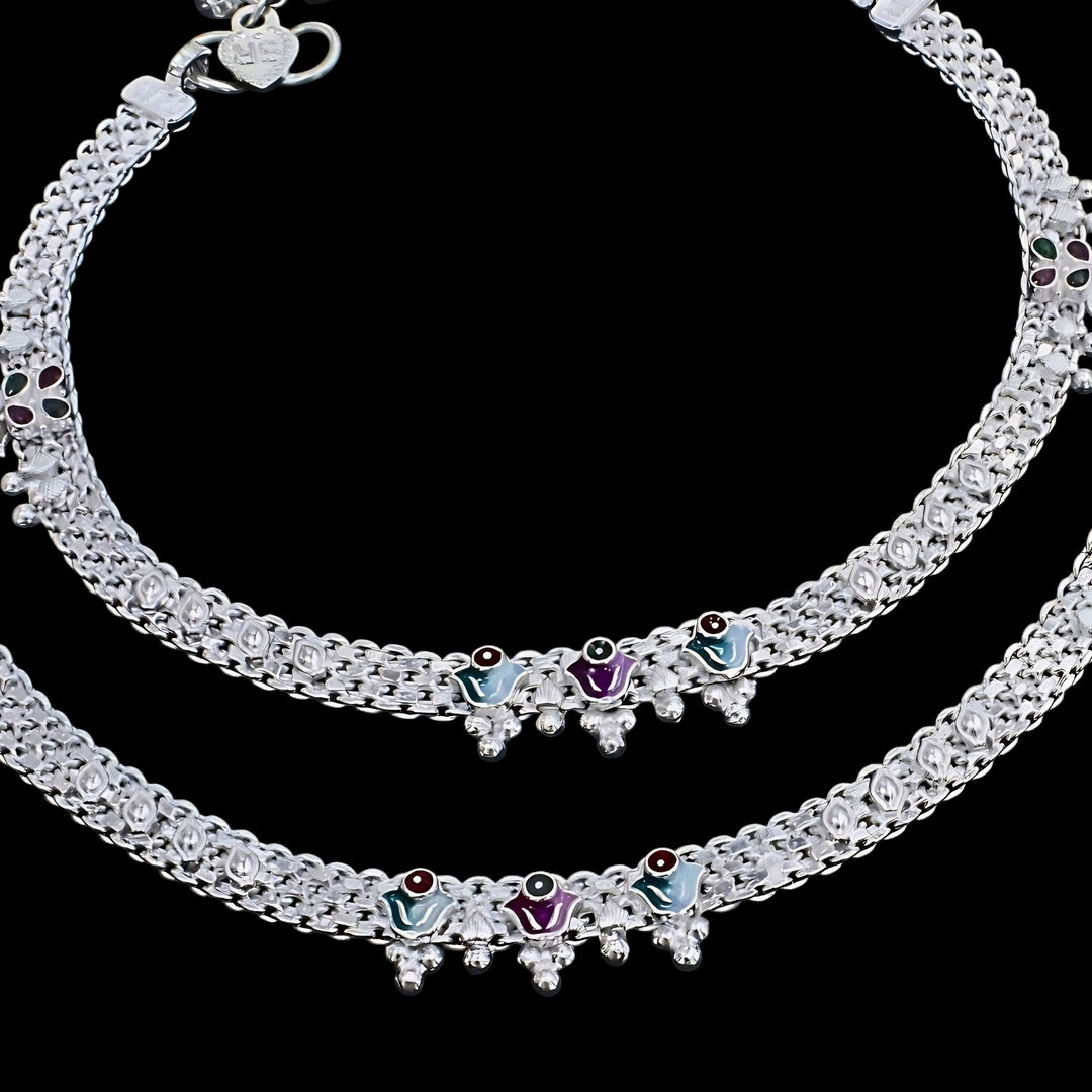 A close-up shot of a pair of silver anklets (payal) arranged in curves against a solid black background.