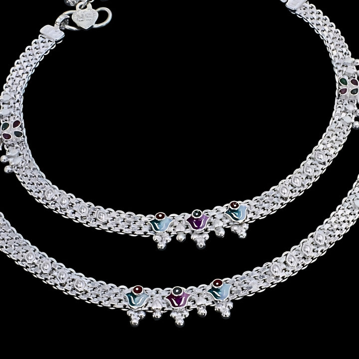 A close-up shot of a pair of silver anklets (payal) arranged in curves against a solid black background.