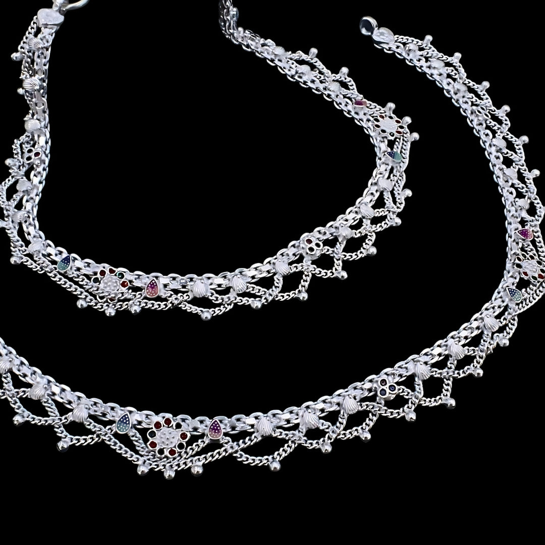 Intricately crafted silver anklets with multi-layered chains, floral enamel motifs, and ghungroo beads showcased against a black background.