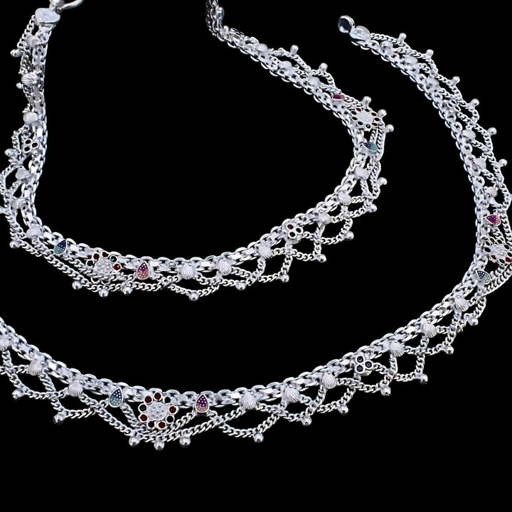 Intricately crafted silver anklets with multi-layered chains, floral enamel motifs, and ghungroo beads showcased against a black background.