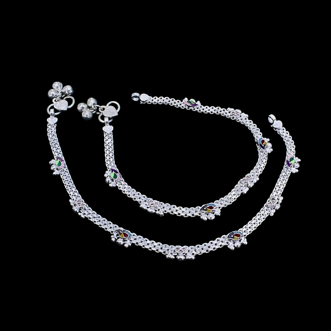 A pair of silver anklets with colorful enamel designs and small bells, displayed against a solid black background.