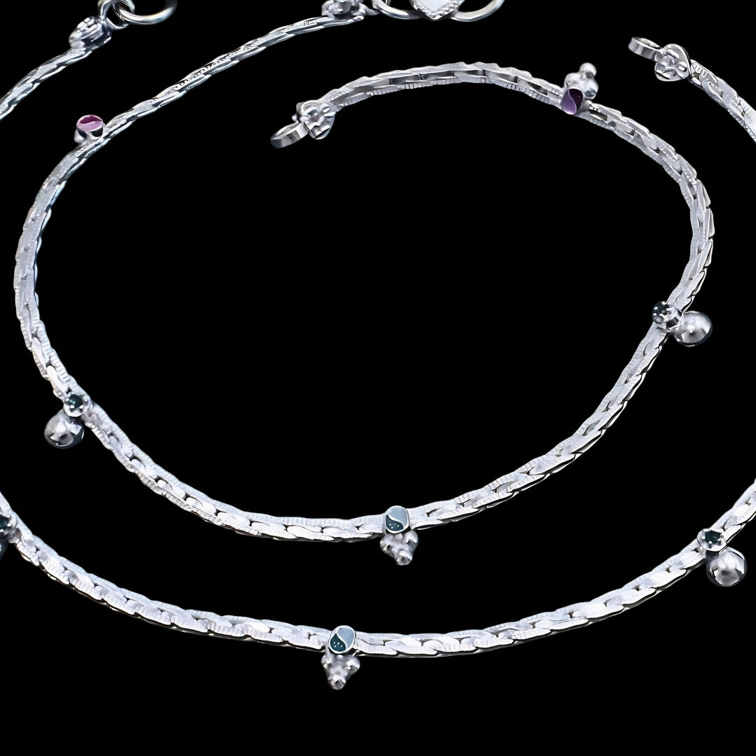 Elegant silver anklet with ghungroo bells and blue enamel charms showcased on a black background.