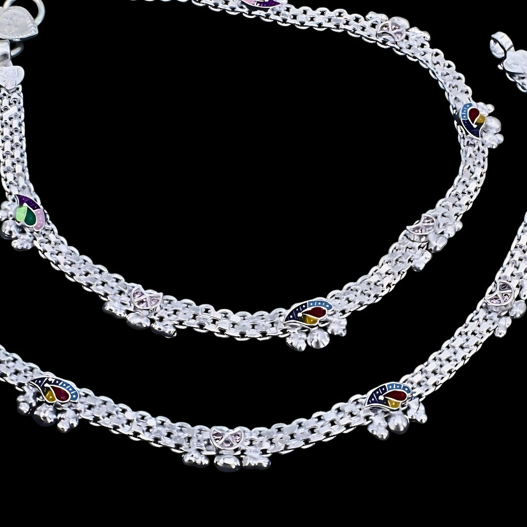 Silver anklets with woven chains and colorful mango-shaped enamel charms on a black background.