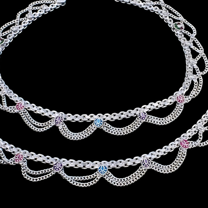 Two silver anklet chains with decorative colored charms on a black background.