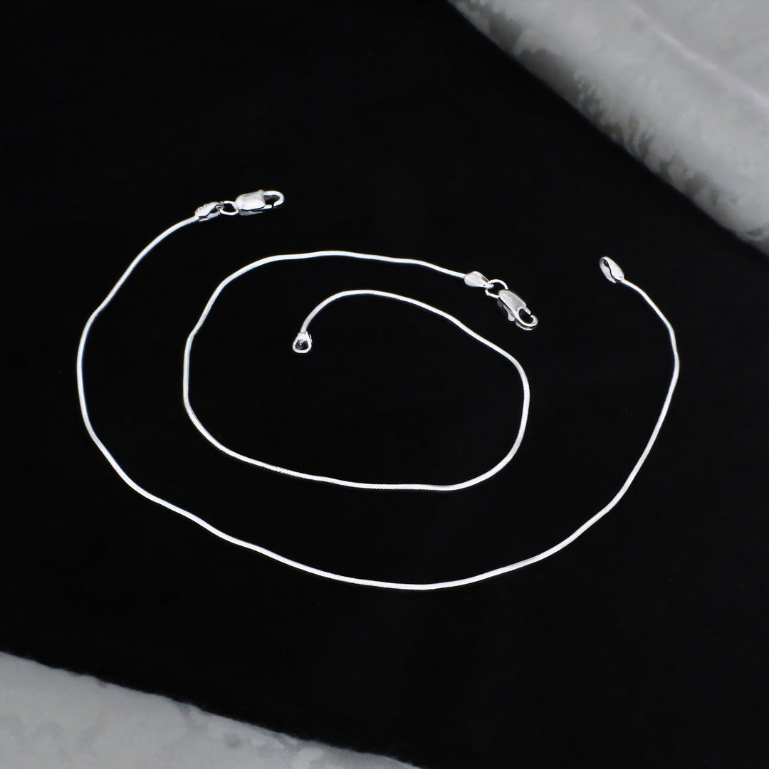A sleek silver snake chain anklet with lobster claw clasps, elegantly displayed in a loose spiral on a black background for a premium, stylish look.
