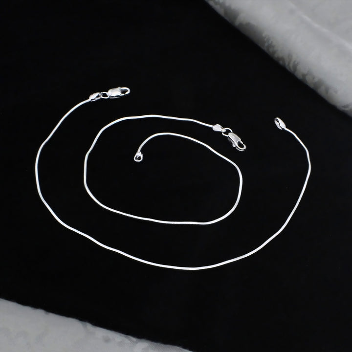 A sleek silver snake chain anklet with lobster claw clasps, elegantly displayed in a loose spiral on a black background for a premium, stylish look.