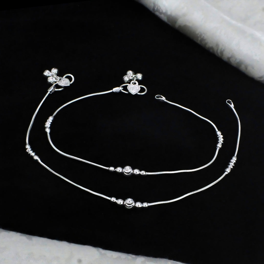 Elegant silver snake chain anklets featuring delicate bead accents, a central round charm, and a heart-shaped clasp for a stylish and graceful look.