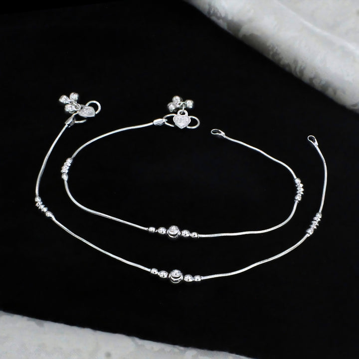 Elegant silver snake chain anklets featuring delicate bead accents, a central round charm, and a heart-shaped clasp for a stylish and graceful look.