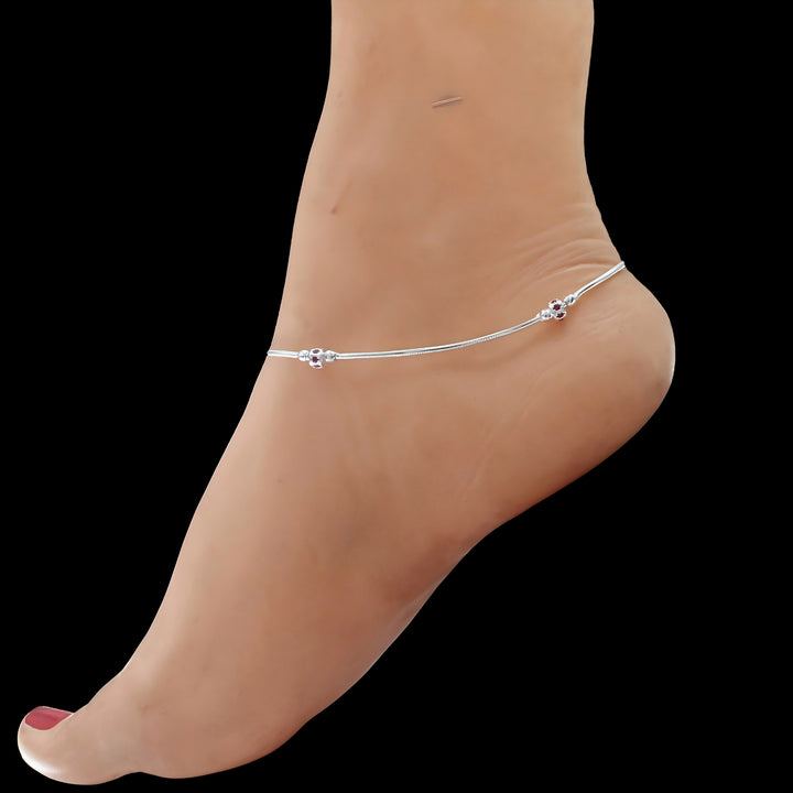 This image shows a person's foot and ankle wearing a silver chain anklet against a plain black background.