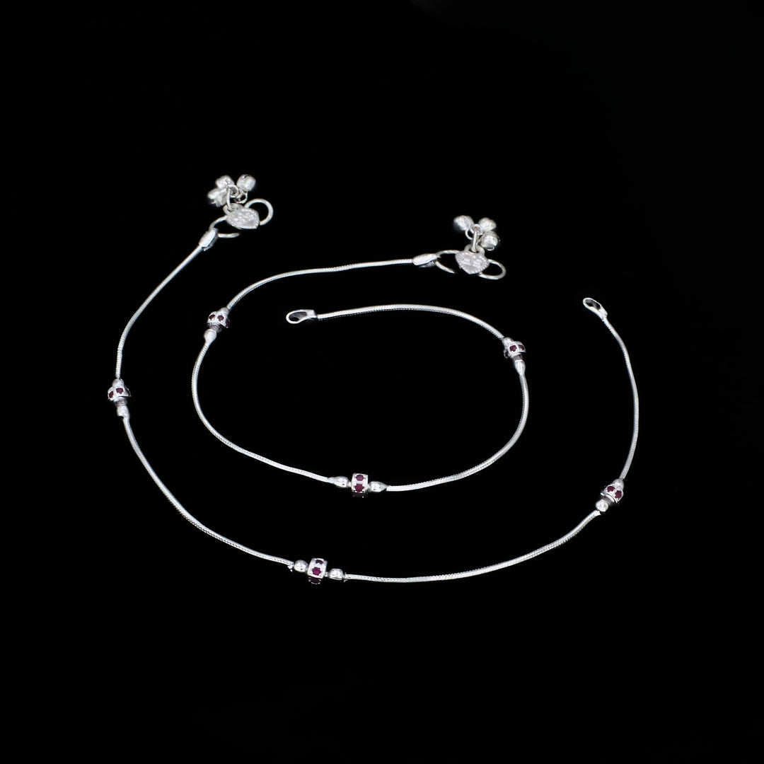 A pair of silver anklets and a matching silver bracelet arranged against a solid black background.