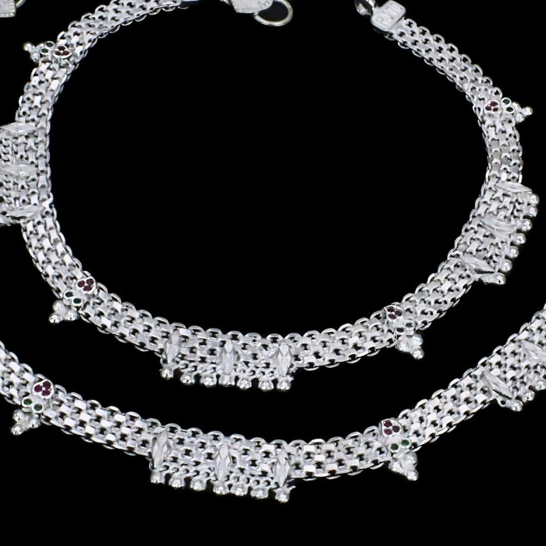 A close-up shot of a pair of traditional Indian silver anklets, known as anklet, displayed against a solid black background.