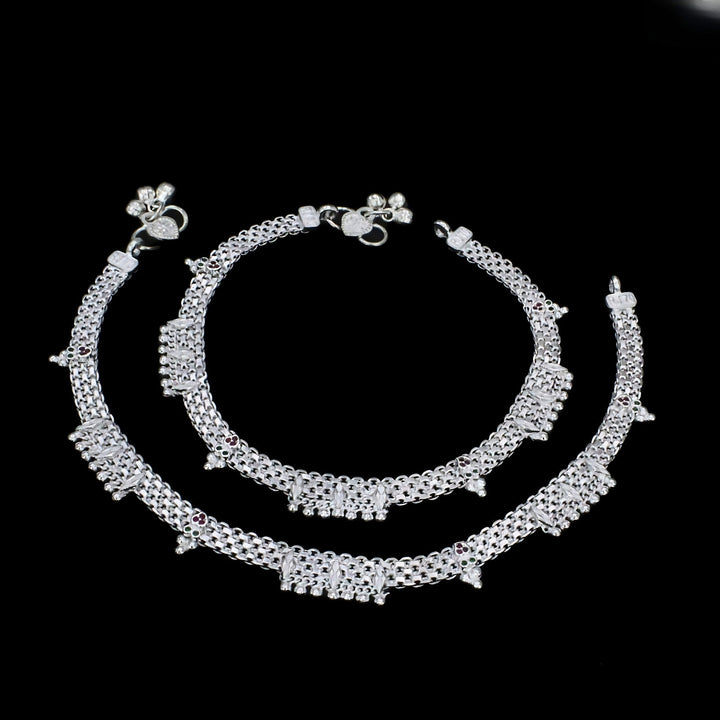 A pair of intricate silver anklets, known as payal, displayed against a solid black background.