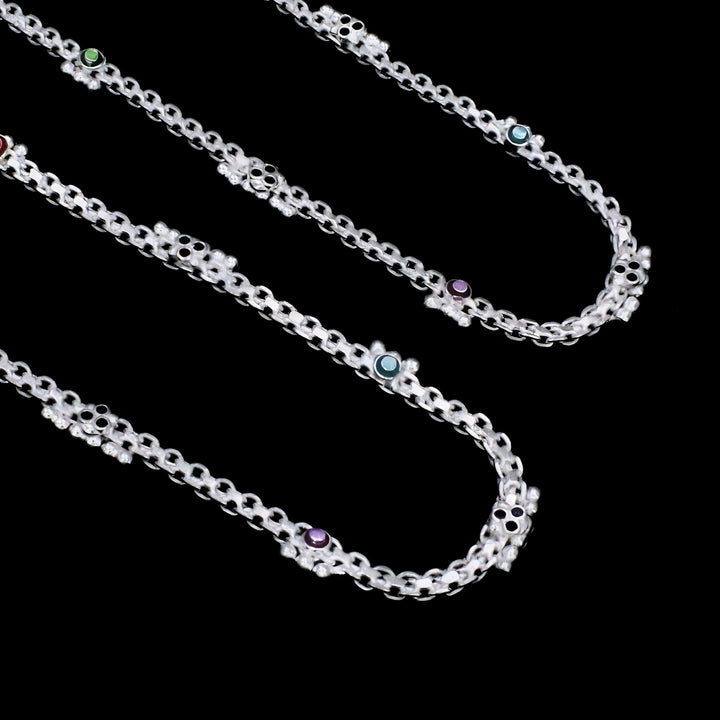 A black background with three silver chains featuring small, colored stones.