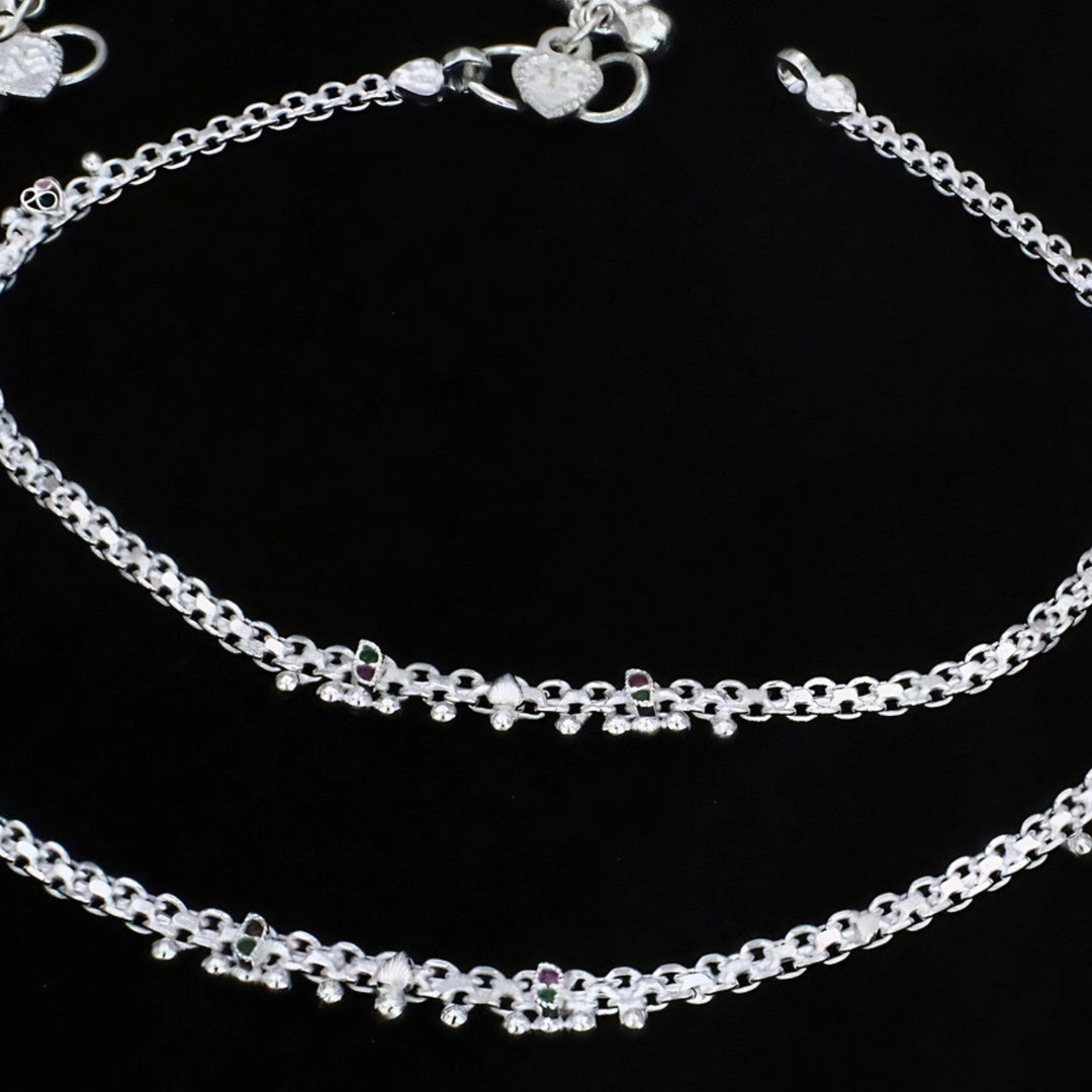 A detailed close-up shot shows delicate, silver  anklets with intricate links and tiny decorative beads, neatly arranged on a solid black background.