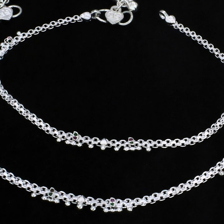 A detailed close-up shot shows delicate, silver  anklets with intricate links and tiny decorative beads, neatly arranged on a solid black background.
