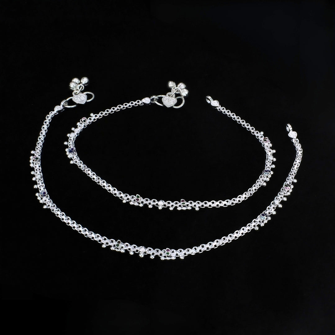 An image shows two ornate silver chain anklets arranged in concentric curves against a solid black background.