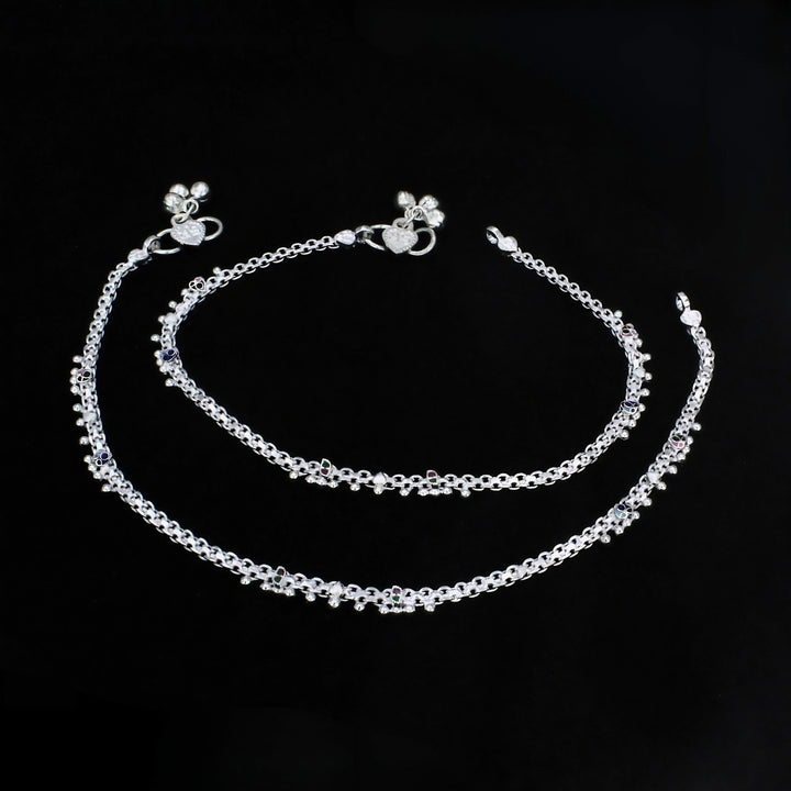 An image shows two ornate silver chain anklets arranged in concentric curves against a solid black background.