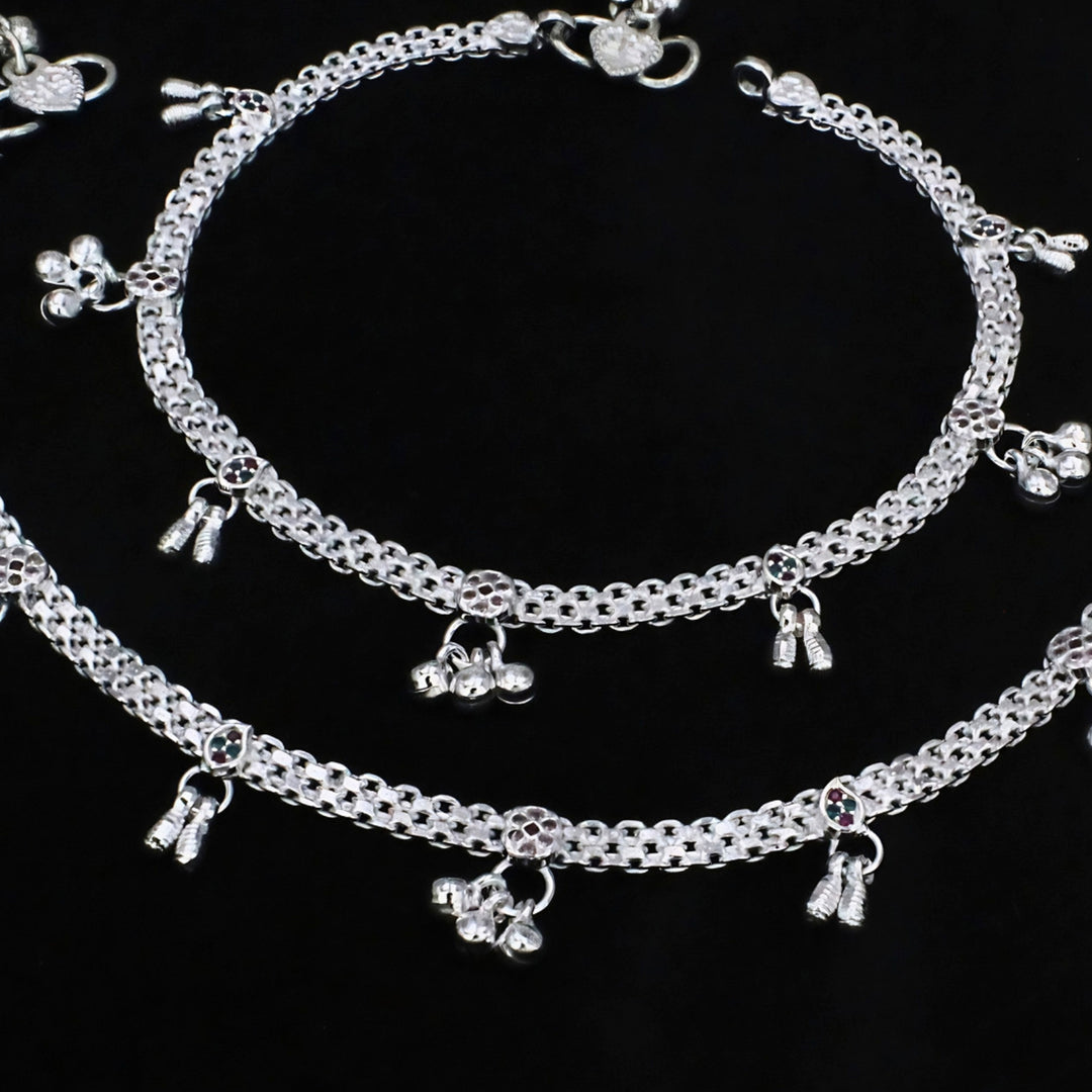 An overhead shot of two shiny silver anklets, known as payal, displayed against a solid black background.