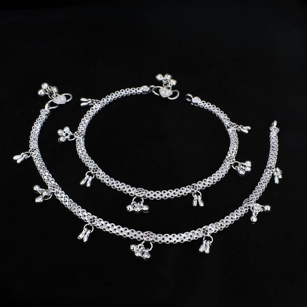A pair of silver Indian anklets, known as payal, displayed against a solid black background.