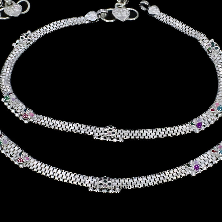This picture shows a pair of silver anklets. They are set against a solid black background.