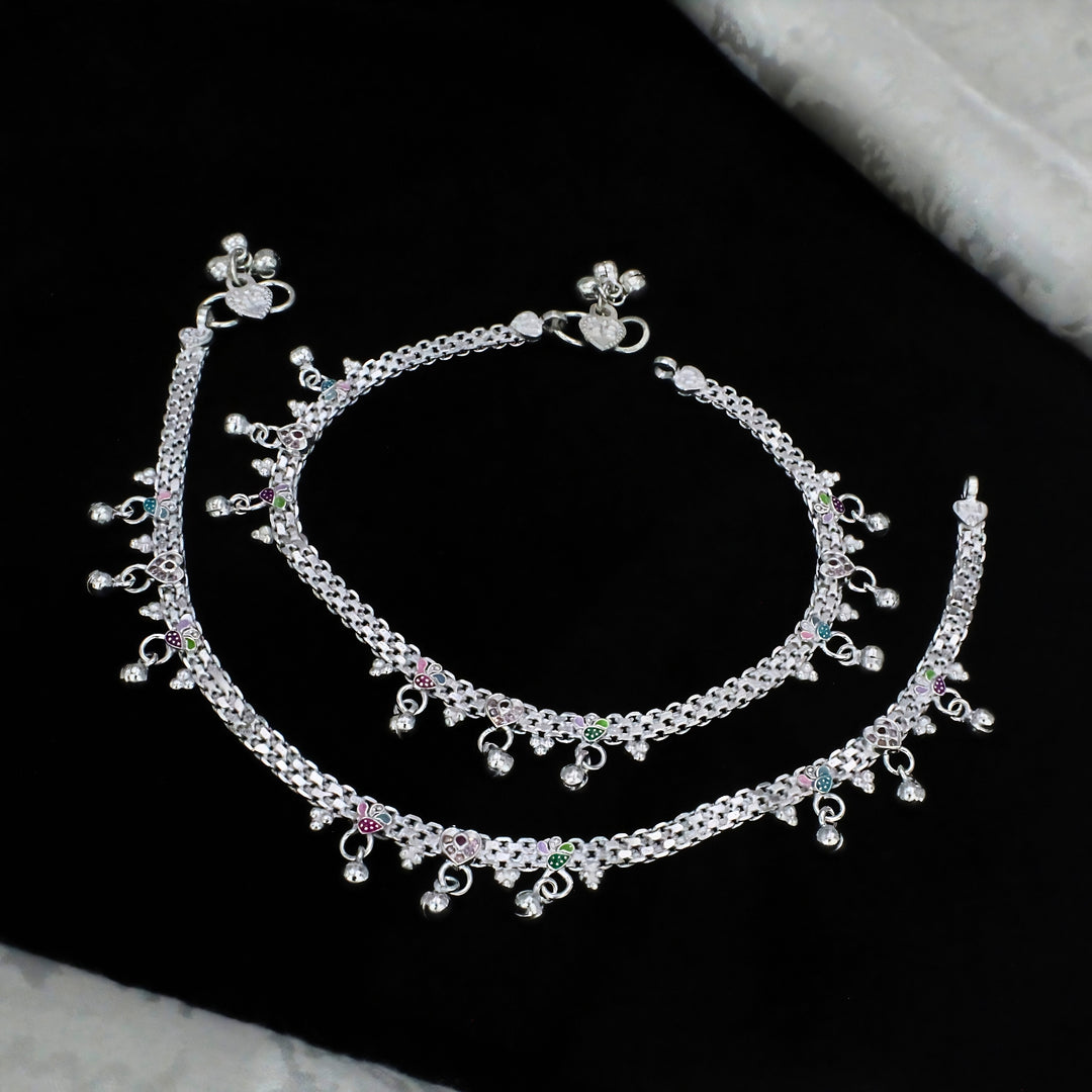 A pair of intricately designed silver payal anklets featuring detailed chain links, dangling charms, and subtle colorful enamel accents for an elegant traditional look.