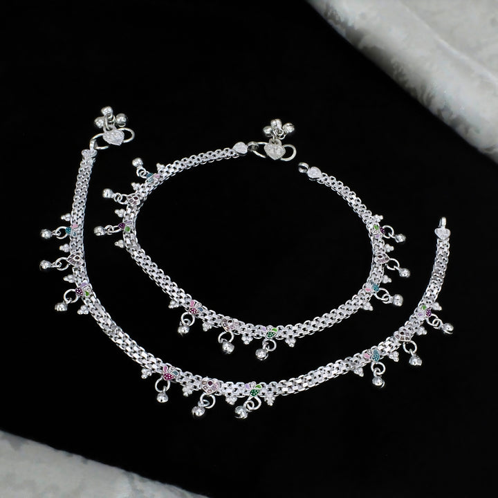 A pair of intricately designed silver payal anklets featuring detailed chain links, dangling charms, and subtle colorful enamel accents for an elegant traditional look.