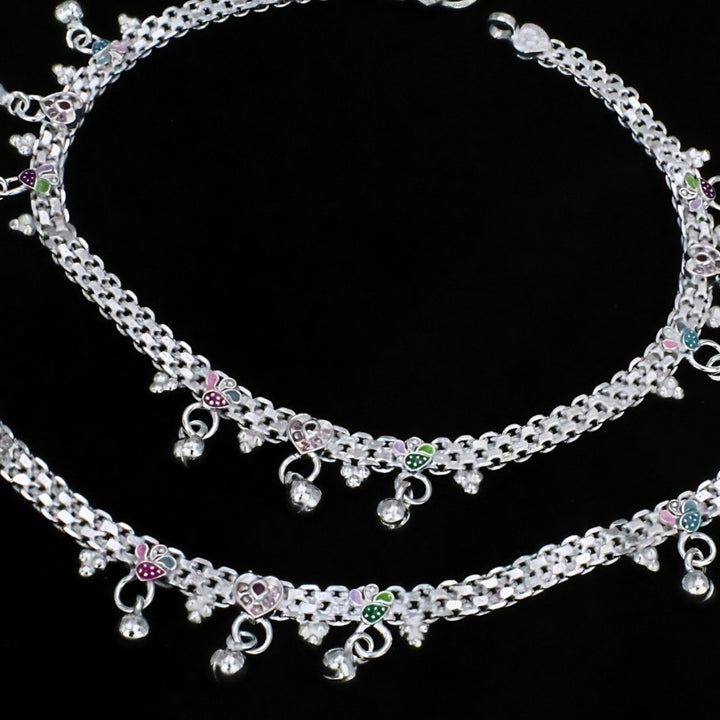 Two silver anklets with colorful leaf charms and small hanging bells are displayed against a black background.
