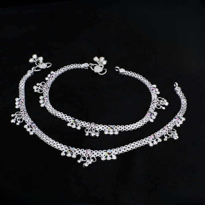 A pair of intricately designed silver payal anklets featuring detailed chainwork, colorful enamel accents, and dangling jingle bells, elegantly displayed against a solid black background.
