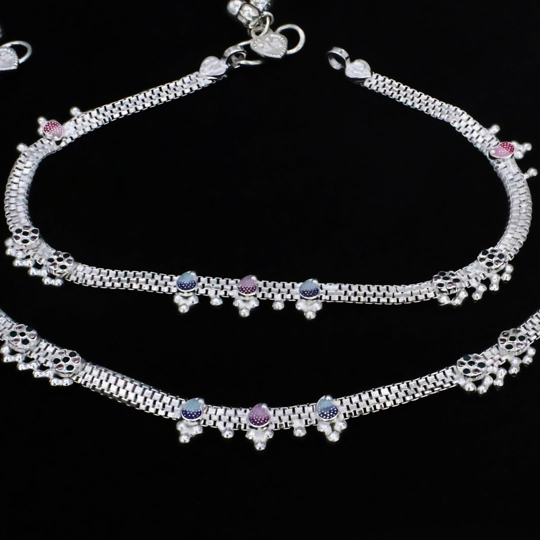 A pair of silver anklets with colorful accents against a solid black background.