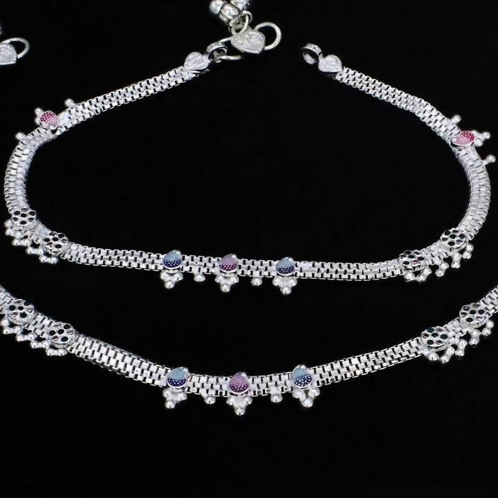 A pair of silver anklets with colorful accents against a solid black background.