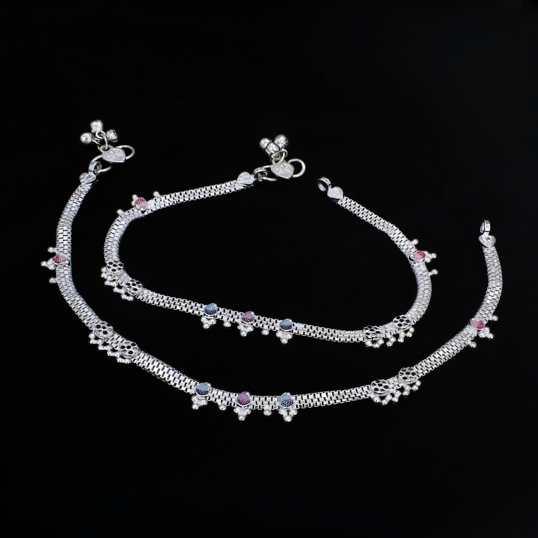 An overhead shot of a pair of traditional Indian silver anklets, known as payal, displayed against a solid black background.