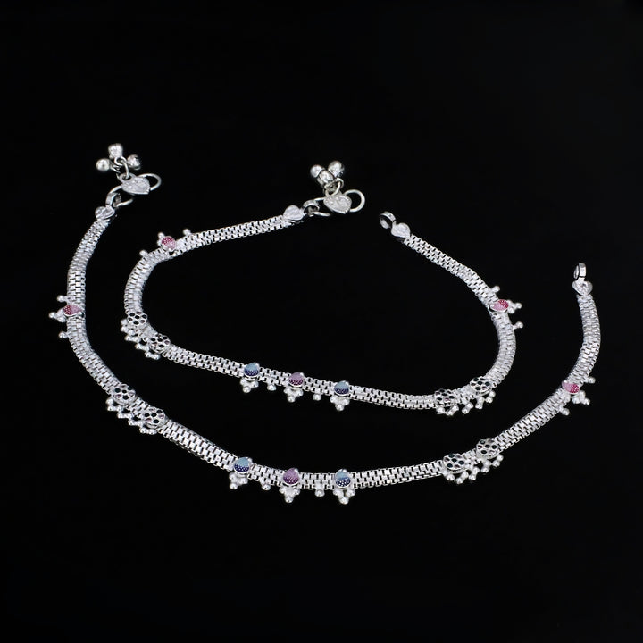 An overhead shot of a pair of traditional Indian silver anklets, known as payal, displayed against a solid black background.